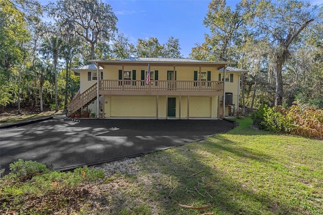view of property with metal roof, an attached garage, stairs, a front yard, and driveway