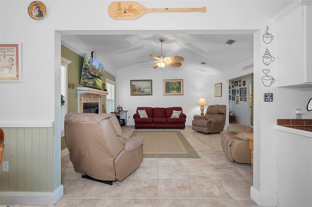 living area with lofted ceiling, light tile patterned flooring, visible vents, a ceiling fan, and a glass covered fireplace