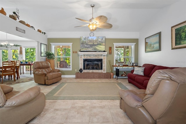 living area with light tile patterned flooring, a wealth of natural light, a tiled fireplace, and ceiling fan with notable chandelier