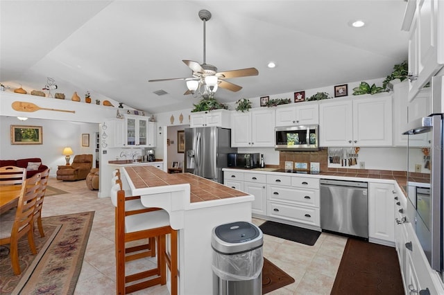kitchen with tile counters, lofted ceiling, black appliances, and white cabinetry