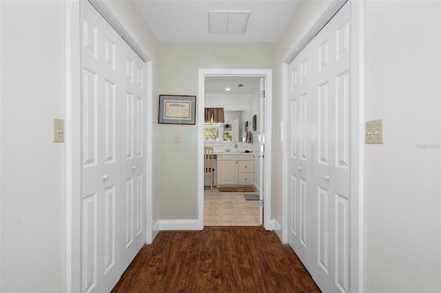 hallway with dark wood-style flooring, a sink, baseboards, and visible vents