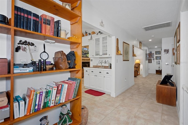corridor with light tile patterned flooring, a sink, baseboards, and visible vents