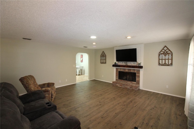living room featuring dark wood finished floors, a brick fireplace, arched walkways, and visible vents