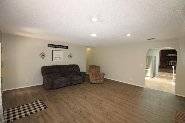 living area featuring baseboards, wood finished floors, arched walkways, and a textured ceiling