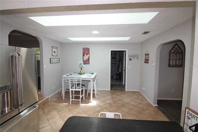 dining room with baseboards, arched walkways, a skylight, and light tile patterned floors