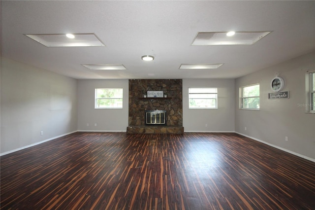 unfurnished living room with a stone fireplace, baseboards, wood finished floors, and plenty of natural light