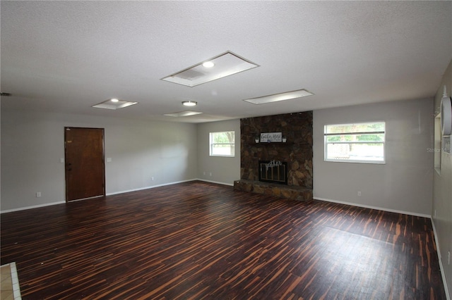 unfurnished living room featuring a stone fireplace, a wealth of natural light, wood finished floors, and baseboards