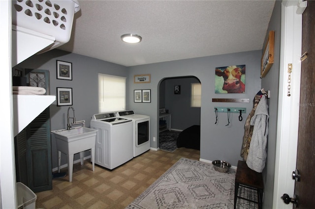laundry area featuring washer and clothes dryer, a textured ceiling, arched walkways, laundry area, and light floors