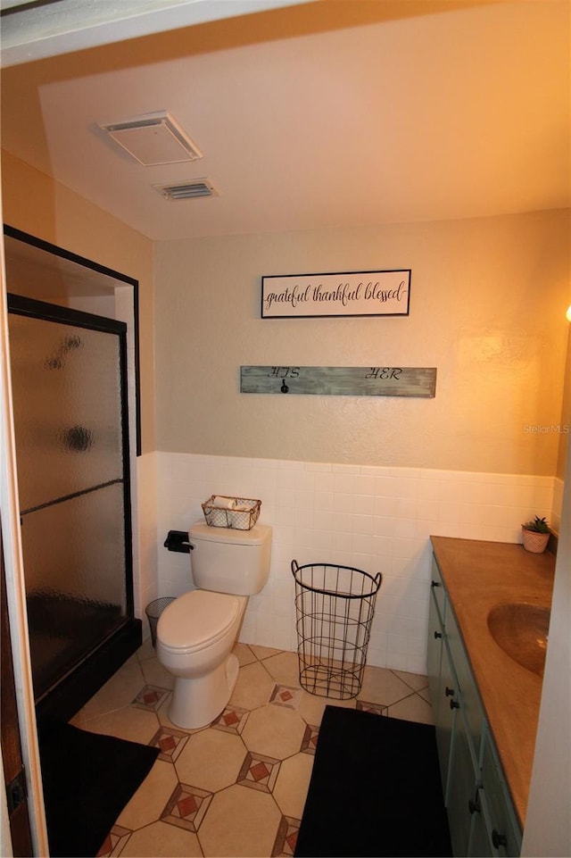 bathroom with tile walls, a wainscoted wall, visible vents, vanity, and a stall shower