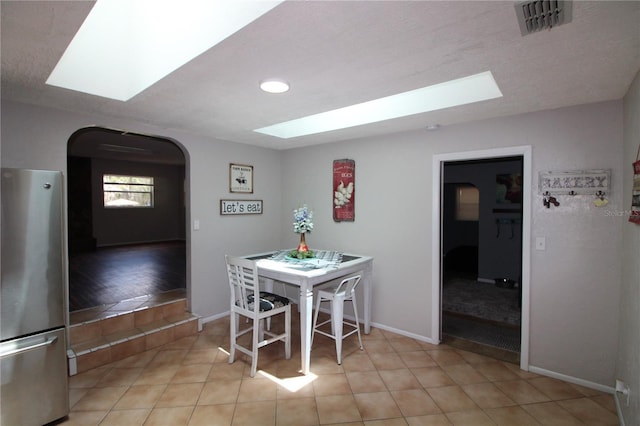 dining space with arched walkways, a skylight, baseboards, and visible vents