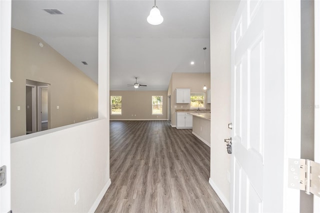 hallway featuring baseboards, lofted ceiling, visible vents, and wood finished floors