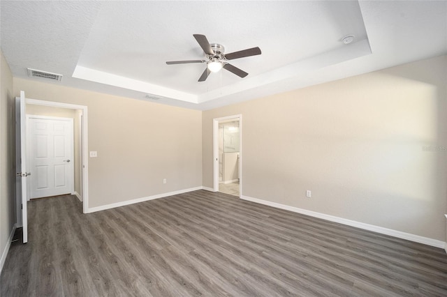 unfurnished room featuring a tray ceiling, baseboards, visible vents, a ceiling fan, and wood finished floors