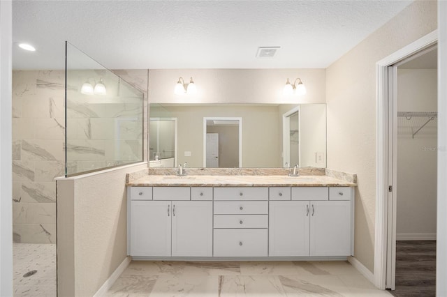 bathroom with marble finish floor, a sink, visible vents, double vanity, and a walk in shower