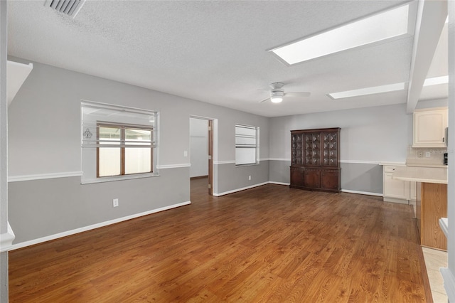 8645 SW 94th Ln Unit E, Ocala, FL 34481 - unfurnished living room featuring baseboards, visible vents, ceiling fan, a skylight, and wood finished floors