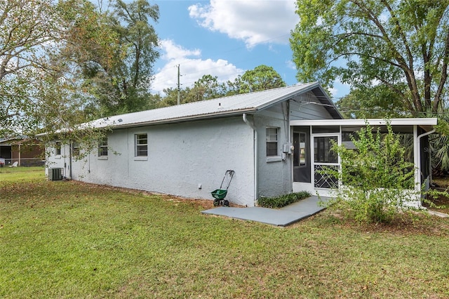 6830 NW 62nd Pl, Ocala, FL 34482 - rear view of house featuring a sunroom, stucco siding, metal roof, central AC unit, and a lawn