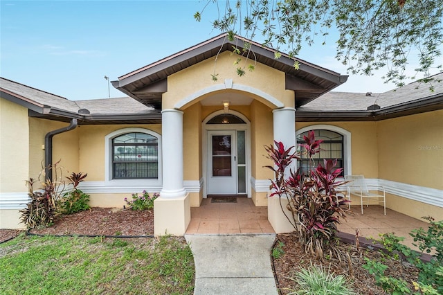 view of exterior entry featuring stucco siding and a shingled roof