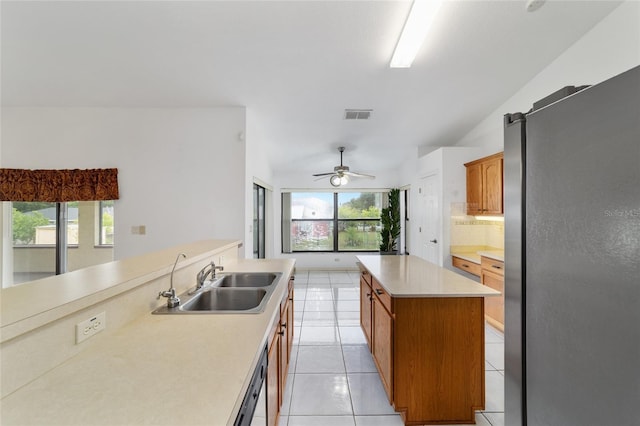 kitchen with freestanding refrigerator, a sink, a center island, light tile patterned floors, and light countertops