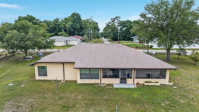 back of house featuring a lawn, a sunroom, stucco siding, and roof with shingles