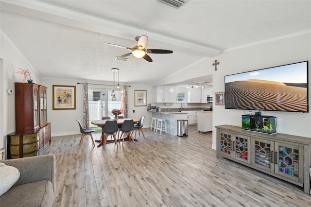 dining area featuring a textured ceiling, baseboards, ceiling fan, light wood-style floors, and vaulted ceiling with beams