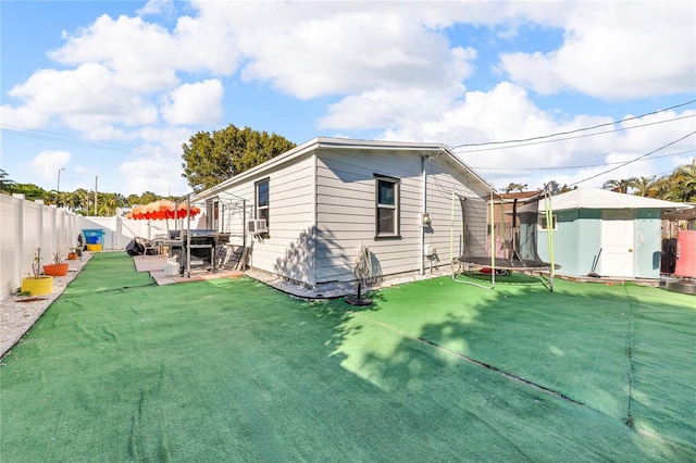 rear view of property featuring a trampoline, a fenced backyard, a lawn, and a patio