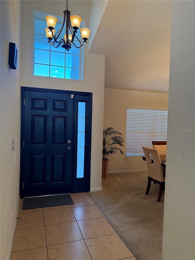tiled entryway featuring a chandelier, baseboards, and carpet floors