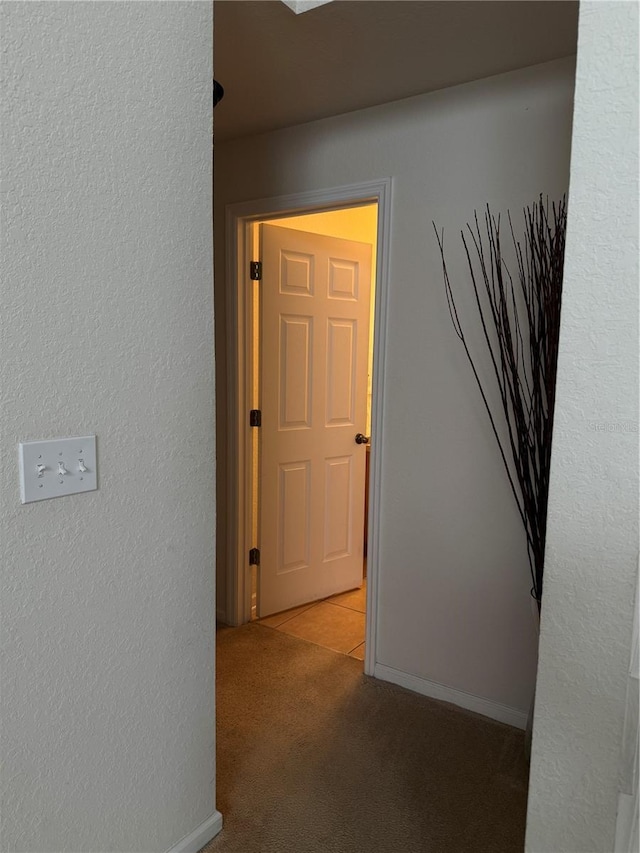 hallway featuring carpet, a textured wall, and baseboards