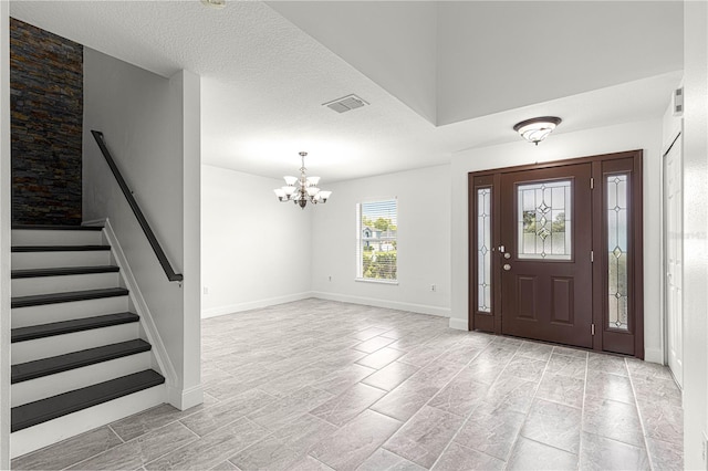 entrance foyer with an inviting chandelier, a textured ceiling, stairs, and visible vents