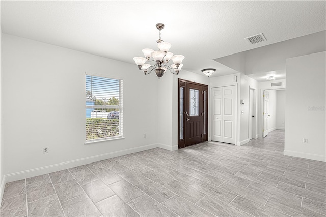 interior space with baseboards, a textured ceiling, visible vents, and an inviting chandelier