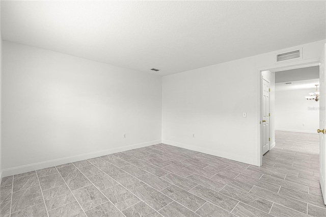 unfurnished room with an inviting chandelier, a textured ceiling, baseboards, and visible vents
