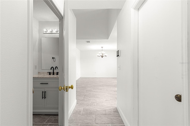hall featuring a sink, baseboards, a chandelier, and visible vents
