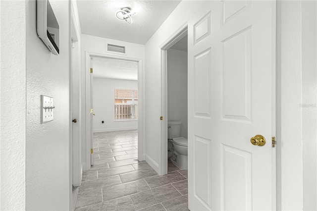 corridor with a textured ceiling, baseboards, and visible vents