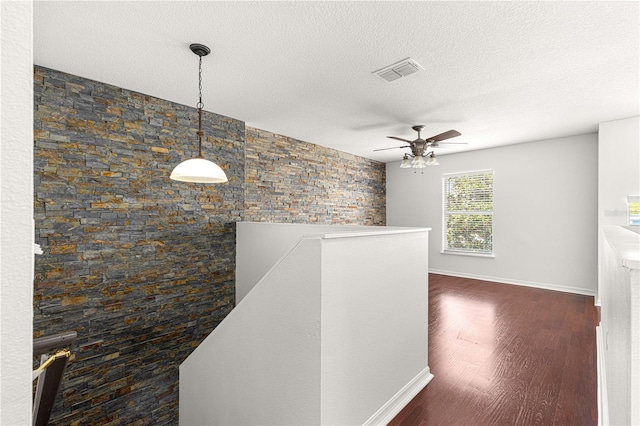 corridor with an upstairs landing, a textured ceiling, baseboards, visible vents, and dark wood-type flooring