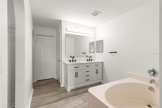full bathroom featuring a closet, a sink, a bath, visible vents, and double vanity