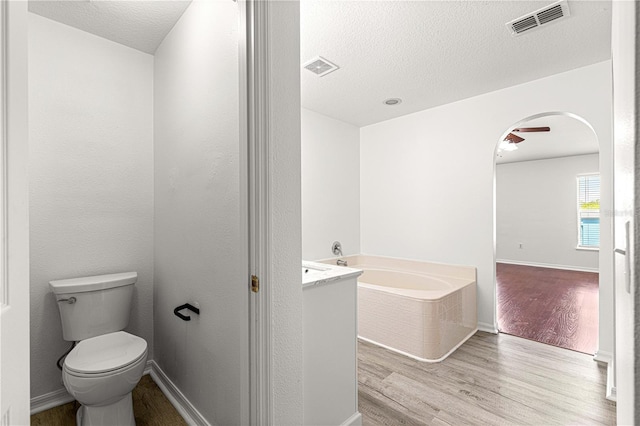 bathroom featuring wood finished floors, toilet, a textured ceiling, visible vents, and a bath