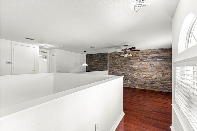 hall featuring an upstairs landing, dark wood-style flooring, a textured ceiling, and visible vents