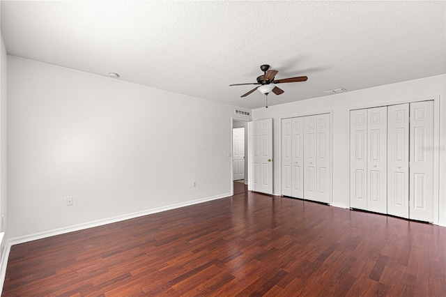 unfurnished bedroom with baseboards, visible vents, two closets, and dark wood-type flooring