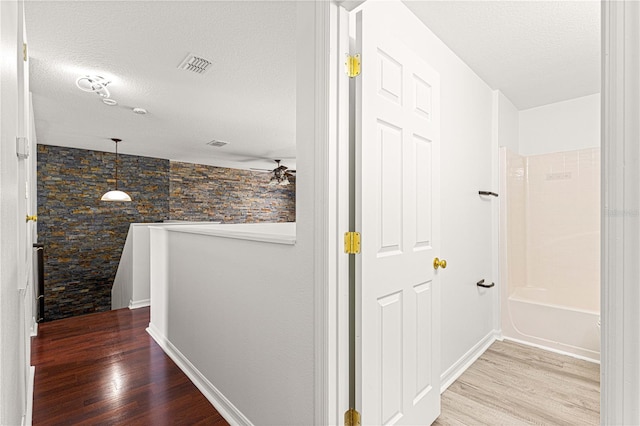 corridor with an upstairs landing, baseboards, a textured ceiling, visible vents, and wood finished floors