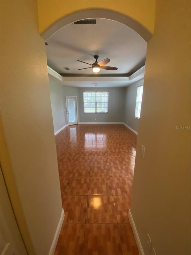 5323 SW 111th Lane Rd, Ocala, FL 34476 - tiled empty room with arched walkways, ceiling fan, a tray ceiling, baseboards, and crown molding