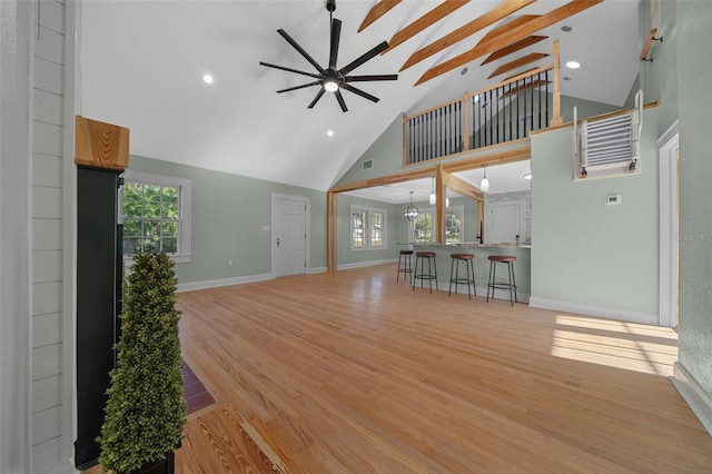 unfurnished living room featuring high vaulted ceiling, ceiling fan, healthy amount of natural light, baseboards, and light wood finished floors