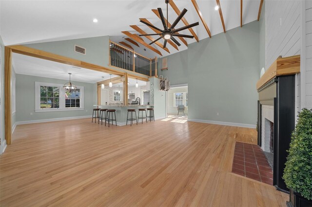 unfurnished living room featuring high vaulted ceiling, a fireplace with flush hearth, ceiling fan, baseboards, and light wood finished floors