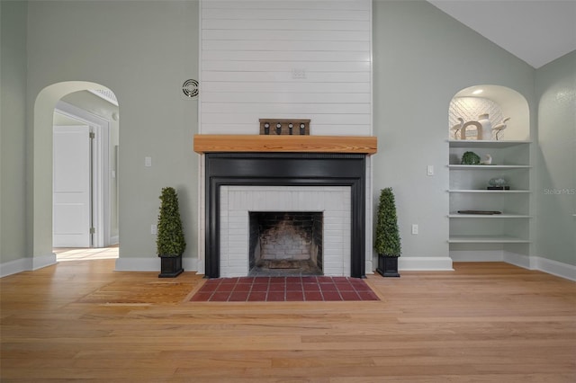 living room with wood finished floors, high vaulted ceiling, a large fireplace, baseboards, and arched walkways