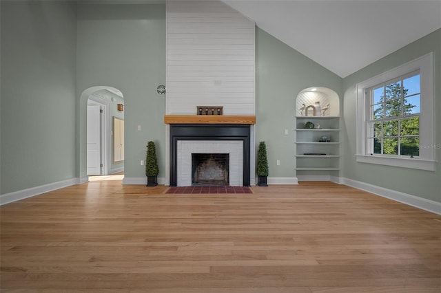 unfurnished living room featuring high vaulted ceiling, a fireplace, light wood-type flooring, arched walkways, and baseboards