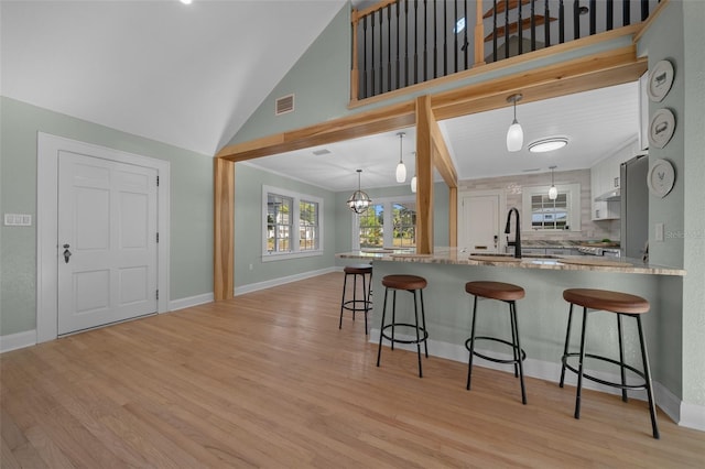 kitchen featuring a breakfast bar, a sink, light wood-style flooring, and high vaulted ceiling