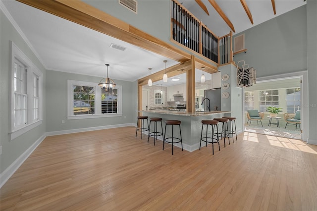 kitchen with a chandelier, a kitchen bar, light wood-style flooring, baseboards, and ornamental molding