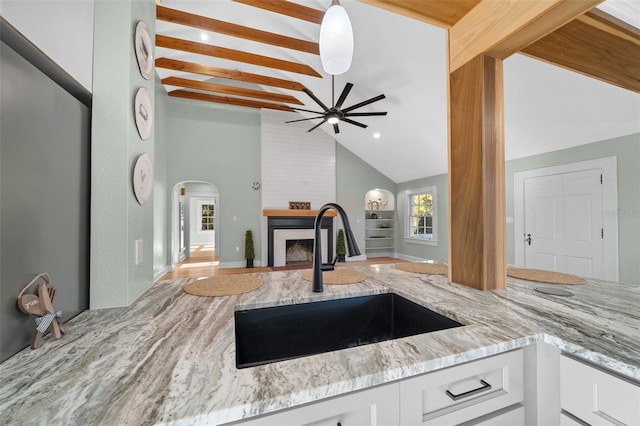 kitchen featuring a sink, a fireplace, white cabinets, and light stone counters