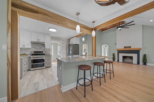 kitchen featuring appliances with stainless steel finishes, light wood-type flooring, a breakfast bar, a sink, and light stone counters