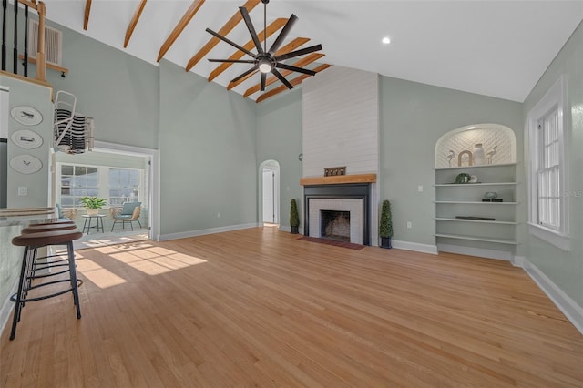 unfurnished living room with high vaulted ceiling, wood finished floors, a fireplace, a ceiling fan, and baseboards