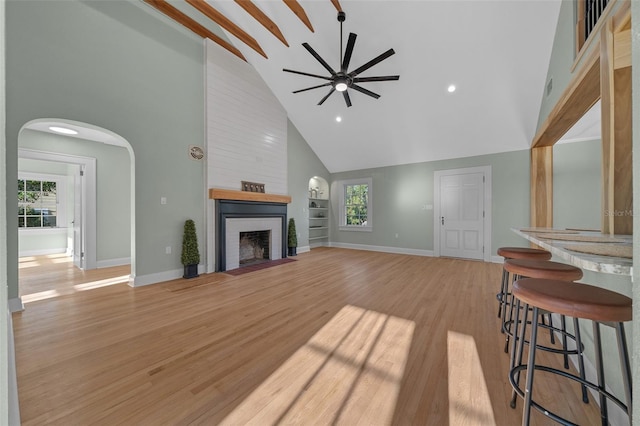 unfurnished living room with high vaulted ceiling, ceiling fan, plenty of natural light, baseboards, and light wood-style floors