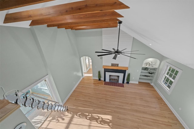 unfurnished living room featuring high vaulted ceiling, beam ceiling, light wood-style floors, a ceiling fan, and a fireplace with flush hearth