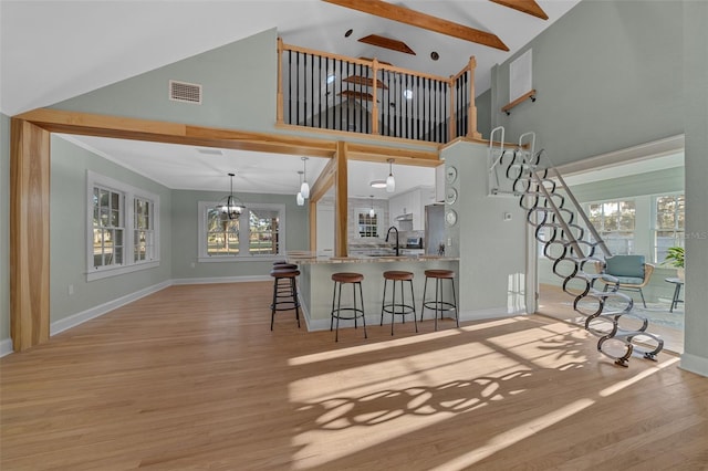 kitchen with high vaulted ceiling, a kitchen breakfast bar, light wood-style flooring, a peninsula, and baseboards